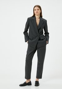 Antraciet grijs dubbelgebreid blazer met brede revers, gecombineerd met gestreepte broek. Gladde stof, nauwsluitende pasvorm en zwarte loafers.