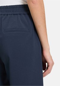 Pantaloni della tuta blu navy con vita elastica, dotati di una tasca posteriore e texture di tessuto leggera e liscia. Design essenziale senza decorazioni.