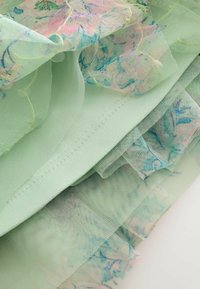 Világoszöld szövet áttetsző, virágmintás réteggel, rózsaszín és kék mintákkal díszítve. Az anyag puha, könnyű, finom szélekkel.