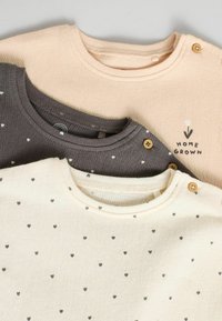 Tres camisetas de manga larga de suave algodón: rosa claro, gris con pequeños corazones y crema con corazones grises; presenta detalles de botones en la camiseta gris.