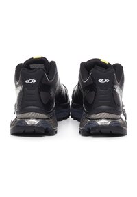 Baskets de sport noires avec un dessus en mesh texturé, talon renforcé et semelle rembourrée, dotées d'un logo réfléchissant et d'un accent jaune.