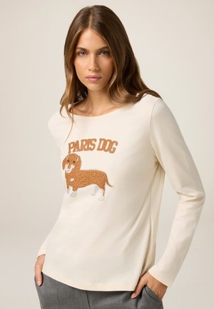 Chemise à manches longues de couleur crème en tissu doux, ornée d'un chien teckel brodé avec le texte "PARIS DOG" au-dessus en fil marron.