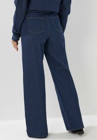 Jeans en denim bleu marine à taille large, avec deux poches arrière et des coutures contrastantes, une texture lisse et une silhouette droite.
