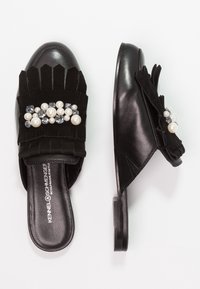 Svarta slip-on skor med övre i mocka, fransdetaljer samt utsmyckning av pärlor och rhinstenar på en platt sula.