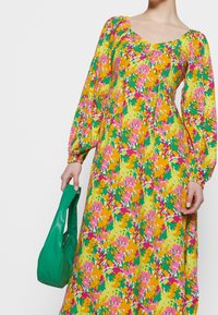 Maxiklänning med blommönster i gula, rosa, gröna och orange nyanser. Långa, puffiga ärmar; fyrkantig urringning. Matchas med en grön handväska.