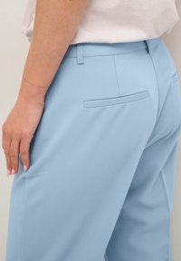 Pantaloni su misura blu chiaro realizzati in tessuto morbido, con tasca posteriore piatta e vita aderente, mostrati di lato.