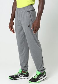 Šedé sportovní kalhoty s tapered střihem, vyrobené z lehké látky. Obsahují boční kapsy a černé logo poblíž pasu.