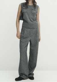 Haut sans manches gris avec un ourlet côtelé et deux poches frontales, associé à un pantalon large gris. La tenue est complétée par des baskets noires.