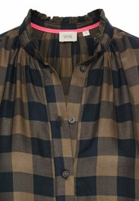 Knoop-up geruite blouse met een houndstooth patroon in donkerblauw en tan, met een gerimpelde kraag en twee zichtbare knopen.