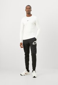 Pitkähihaisen valkoisen urheilupaidan, jossa on musta Nike-logo, parina mustat collegehousut, joissa on valkoinen Nike-grafiikka. Yhdistetty valkoisiin urheilukenkiin.