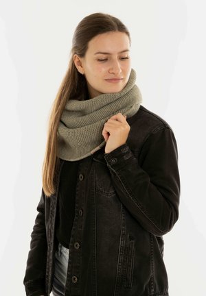 Knitted cowl scarf in soft, light gray with a textured pattern. Worn casually over a black jacket, creating a layered look.
