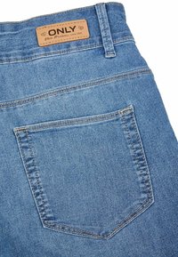 Jeans de mezclilla de color azul claro con una etiqueta de cuero en la cintura que dice "ONLY". Tienen un bolsillo trasero con costuras visibles y una textura suave.