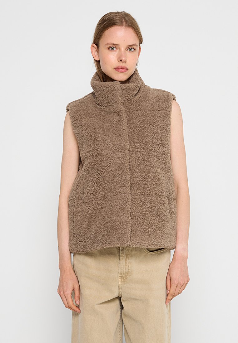 Gilet en polaire marron sans manches avec col montant et poches avant. Texture douce, sans fermetures visibles, design simple. Convient pour le superposition.