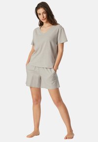 Šedé bavlněné tričko s výstřihem do V a krátkými rukávy, které je kombinováno se šedými šortkami ve stejné barvě. Materiál vypadá měkce, má uvolněný střih a jednoduchý design.
