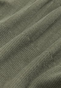 Gros plan sur un tissu en maille côtelée vert olive avec des rayures verticales texturées et des motifs de tricot alternant serré et lâche.