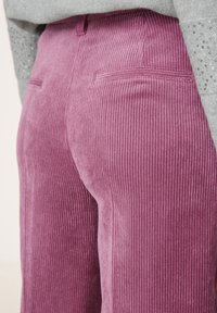 Lila kordflortbyxor med vertikal ribbad textur, med två bakfickor och en åtsittande design. Inga synliga knäppningar eller accenter.