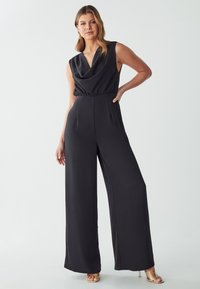 Combinaison noire sans manches avec un décolleté drapé, taille cintrée et design à jambes larges, fabriquée en tissu lisse. Accentuée par un matériel minimal.
