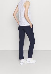 Bílý bezrukávový top s černými skvrnami, spárovaný s námořnickými kalhotami. Bílé tenisky mají světle zelený akcent. Jednoduchý design, přiléhavá silueta.