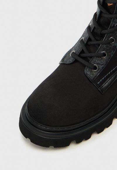 Botte en suede noire avec un accent en cuir texturé, design à lacets et semelle en caoutchouc robuste. Présente des détails de couture contrastés.