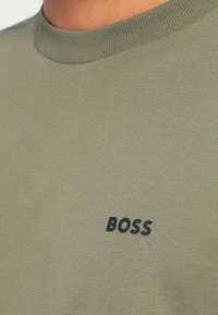 Olíva zöld, kerek nyakú póló sima pamutból, elöl egy kis fekete "BOSS" logóval.