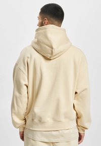Beige oversized hoodie med en stor hætte, ribbede mansjetter og kant. Blødt stof med en glat tekstur, som viser et afslappet fit-design.