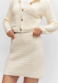 Ensemble cardigan et jupe en maille couleur crème, présentant un motif à carreaux texturé, des boutons ronds et une taille ajustée.