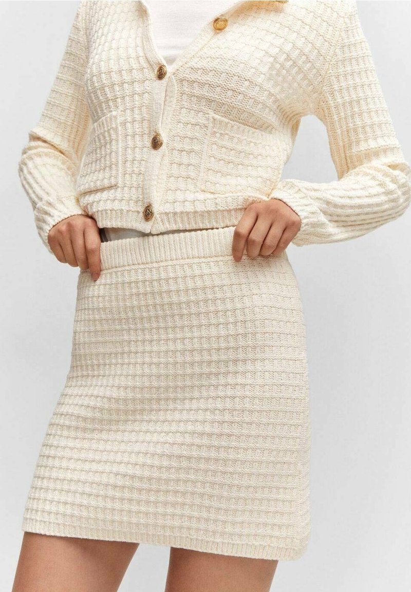 Ensemble cardigan et jupe en maille couleur crème, présentant un motif à carreaux texturé, des boutons ronds et une taille ajustée.