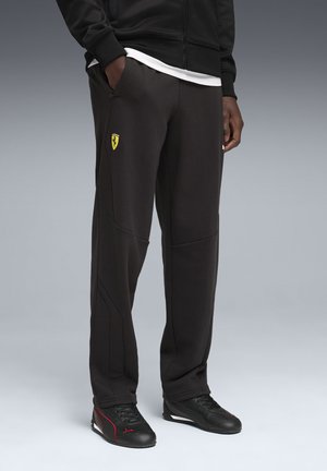 Zwarte joggingbroek van gestructureerde stof, met een geel Ferrari-logo, taps toelopend ontwerp en zijzakken. Gecombineerd met zwarte sportschoenen.