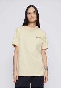 Camiseta de algodón amarilla clara con cuello redondo, mangas cortas y un pequeño diseño impreso que presenta una linterna y texto en el lado izquierdo del pecho.