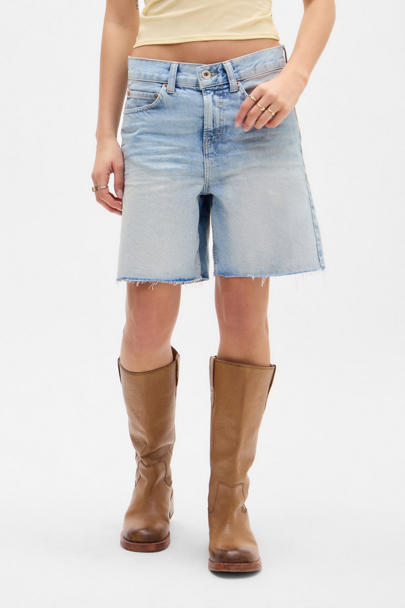 Shorts en denim bleu clair avec un ourlet effiloché, taille mi-haute, associés à des bottes en cuir marron jusqu'aux genoux. Texture lisse, design décontracté.