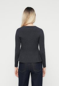 Pull en maille gris foncé ajusté avec des manches longues et un col rond, présentant une texture subtile et un ourlet évasé. Porté avec un jean foncé.