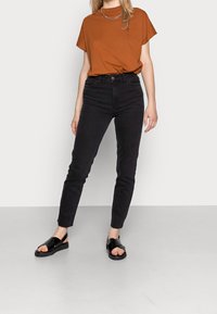 Top corto marrón de manga corta combinado con vaqueros negros de cintura alta y sandalias negras de punta abierta, con una textura suave y un diseño ajustado.