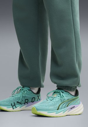 Füße tragen türkise Puma Laufschuhe mit limonengrünen Akzenten und dunkelgrünen Jogginghosen mit elastischen Bündchen.