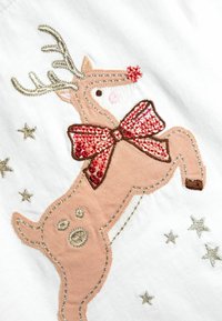 Rénszarvas, piros flitteres masnival és piros orral az fehér anyagon, apró ezüst csillagokkal körülvéve.