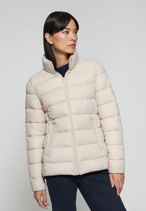 Doudoune beige clair avec texture matelassée, col haut, fermeture éclair et deux poches latérales. Le tissu semble lisse et doux.