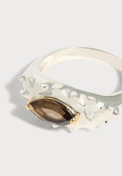 Ασημένιο δαχτυλίδι με υφή στη ζώνη, στο οποίο είναι τοποθετημένη σε χρυσά αγκίστρια μία καπνίζουσα καφέ πολύτιμη πέτρα κομμένη σε σχήμα μαρκίζ.