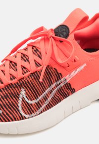 Korálové a černé pletené tenisky s bílým logem Swoosh, texturovaným svrškem, zesílenými dírkami na tkaničky a flexibilní bílou podešví. Šněrovací design.