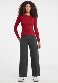 Top aderente rosso a maniche lunghe con scollatura rotonda, abbinato a jeans neri a vita alta con gamba larga e sneakers bianche con strisce nere.