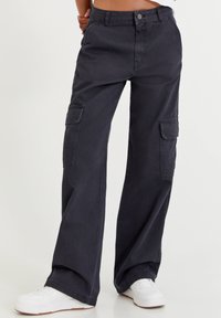 Donkergrijze cargobroek met wijde pijpen, gemaakt van katoen. Bevat voorzakken en zijcargozakken. Gecombineerd met witte sneakers.
