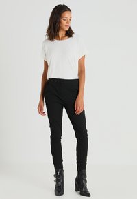 Balta trumpa rankovėmis palaidinė derinama su juodomis siaurėjančiomis kelnėmis ir juodais bateliais su aukštu kulnu, kuriuose yra sagties akcentai. Lygus audinys ir pritaikytas dizainas.