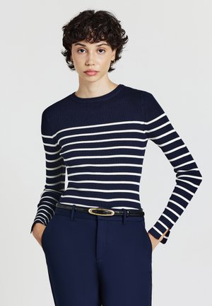 Marineblaues, gestreiftes Langarmoberteil mit weißen horizontalen Streifen; runder Ausschnitt, taillierte Form, kombiniert mit marineblauen Hosen und einem schwarzen Gürtel mit goldener Schnalle.