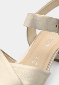 Ανοιχτόχρυση σανδάλι με φαρδιά λουρί και υφή τελείωσης. Περιλαμβάνει ρυθμιζόμενο λουρί αστραγάλου και χαμηλό, κωνικό τακούνι.