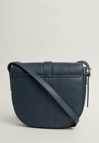 Tamsiai mėlyna odinė crossbody krepšys su apvalia forma, plokščiu viršutinio dangtelio skiriamaisiais ir reguliuojamu dirželiu. Siuvimo detalės prideda subtilaus tekstūros.