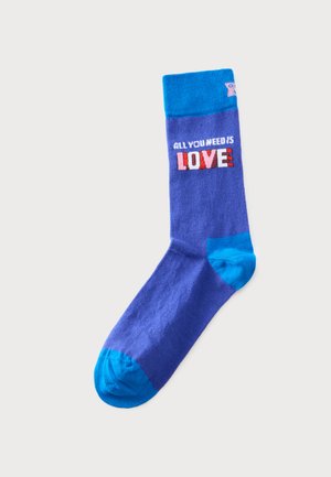 Niebieska skarpetka z jaśniejszym niebieskim piętą, palcem i mankietem, z tekstem "ALL YOU NEED IS LOVE" w białych, różowych i czerwonych literach na mankiecie.