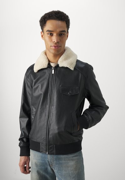 Black leather bomber jacket with a cream-colored shearling collar, zip closure, front pockets, and ribbed cuffs and hem.