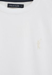 T-shirt blanc à col rond avec petit logo beige de joueur de polo sur la poitrine et une étiquette noire "POLO CLUB" à l'intérieur du col.