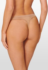 String en dentelle de couleur nude, avec une fine taille et un motif floral à l'arrière, offrant une texture lisse et un design à couverture minimale.