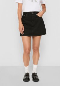 Svart denimskjørt med en tettsittende fasong, frontlommer og knappelukking. Kombinert med en hvit t-skjorte og svarte loafers.