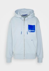 Felpa con cappuccio azzurro chiaro con zip, realizzata in misto cotone. Presenta una tasca frontale, un cappuccio con coulisse e una tasca sul petto blu con testo bianco.