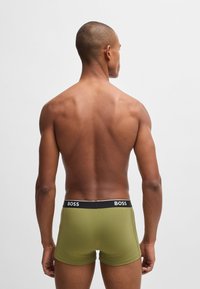 Olivgrüne Boxershorts mit einem schwarzen Bund, der den Markennamen "BOSS" zeigt. Glattes Material und figurbetontes Design. Ansicht von hinten.